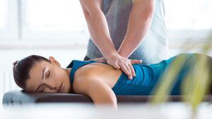 Massage therapist giving back massage to young woman. Patient lying on massage table.