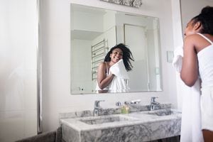 Beautiful black woman drying her face with a towel  in the bathroom while looking at herself in the mirror smiling