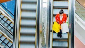 Female shopper standing on escalator with shopping bags in hand.