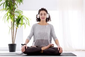 Piernas cruzadas dobladas femeninas delgadas en posición de loto. Una joven atlética con rastreador de fitness y auriculares está practicando yoga, meditando, relajándose mientras se sienta en padma asana en casa.