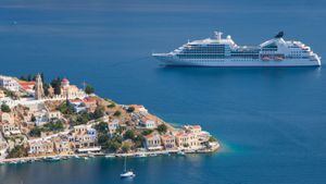 View over colourful rooftops to Harani Bay, cruise ship anchored offshore, Gialos (aka Yialos), Symi (aka Simi), Rhodes, Dodecanese Islands, South Aegean, Greece, Europe.