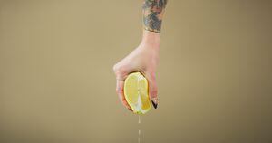 Studio shot of an unrecognizable woman squeezing a lemon slice against a brown background