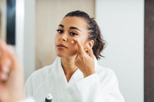 Beautiful woman in bathrobe applying anti-aging cream on her cheek
