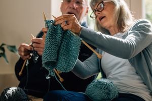 Senior woman teaching her husband the art of knitting woollen clothes. Senior man learning to knit woollen clothes from his wife sitting at home.