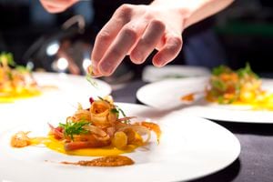 Hand garnishing a plate of poached lobster with carrot crue-cuite