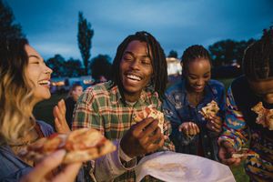 A young group of friends laughing and sharing pizza at a music festival.