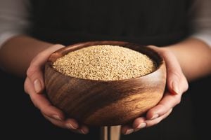 Woman holding wooden bowl with white quinoa on dark background, closeup