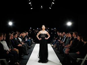 Model in gown walking down catwalk during fashion show photographers and crowd in background