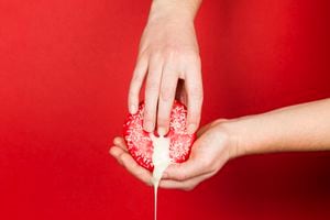 Female hands and a donut on a red background as a symbol of masturbation and foreplay (prelude) before sex. Touch the clitoris, erotic concept.