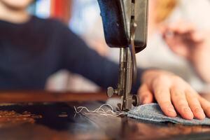 Teenage boy guiding fabric under a vintage sewing machine needle with his mother in the background.
