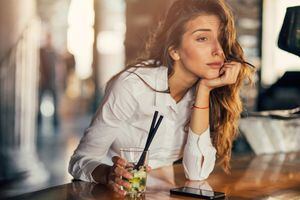 Bored woman drinking cocktail at a bar.