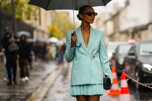 PARIS, FRANCE - OCTOBER 02: A guest wears a black umbrella, black sunglasses, a mint green blazer jacket from Givenchy, a matching mint green pleated / accordion short skirt from Givenchy, a black shiny leather handbag, silver and gold rings, outside Givenchy, during Paris Fashion Week - Womenswear Spring/Summer 2023, on October 02, 2022 in Paris, France. (Photo by Edward Berthelot/Getty Images)