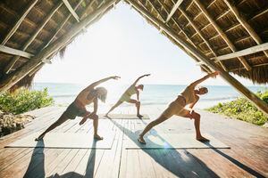 Wide shot of women in extended side angle pose while practicing yoga during class in ocean front pavilion at tropical resort