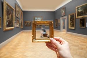 Young man sitting observing a painting framed by golden frame