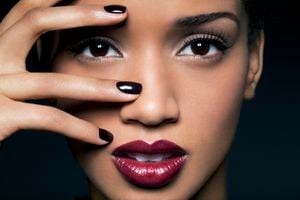 Young African American woman with long lashes, red lips and black nail polish holding her fingers over one of her eyes, close up.