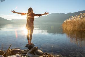 Mujer joven alegre junto al lago disfrutando de la naturaleza. Brazos extendidos por emoción positiva.