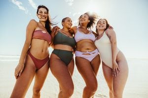 Four girlfriends enjoying beach day together. Group of cheerful young women embracing each other while wearing swimwear. Carefree female friends having fun during their summer vacation.