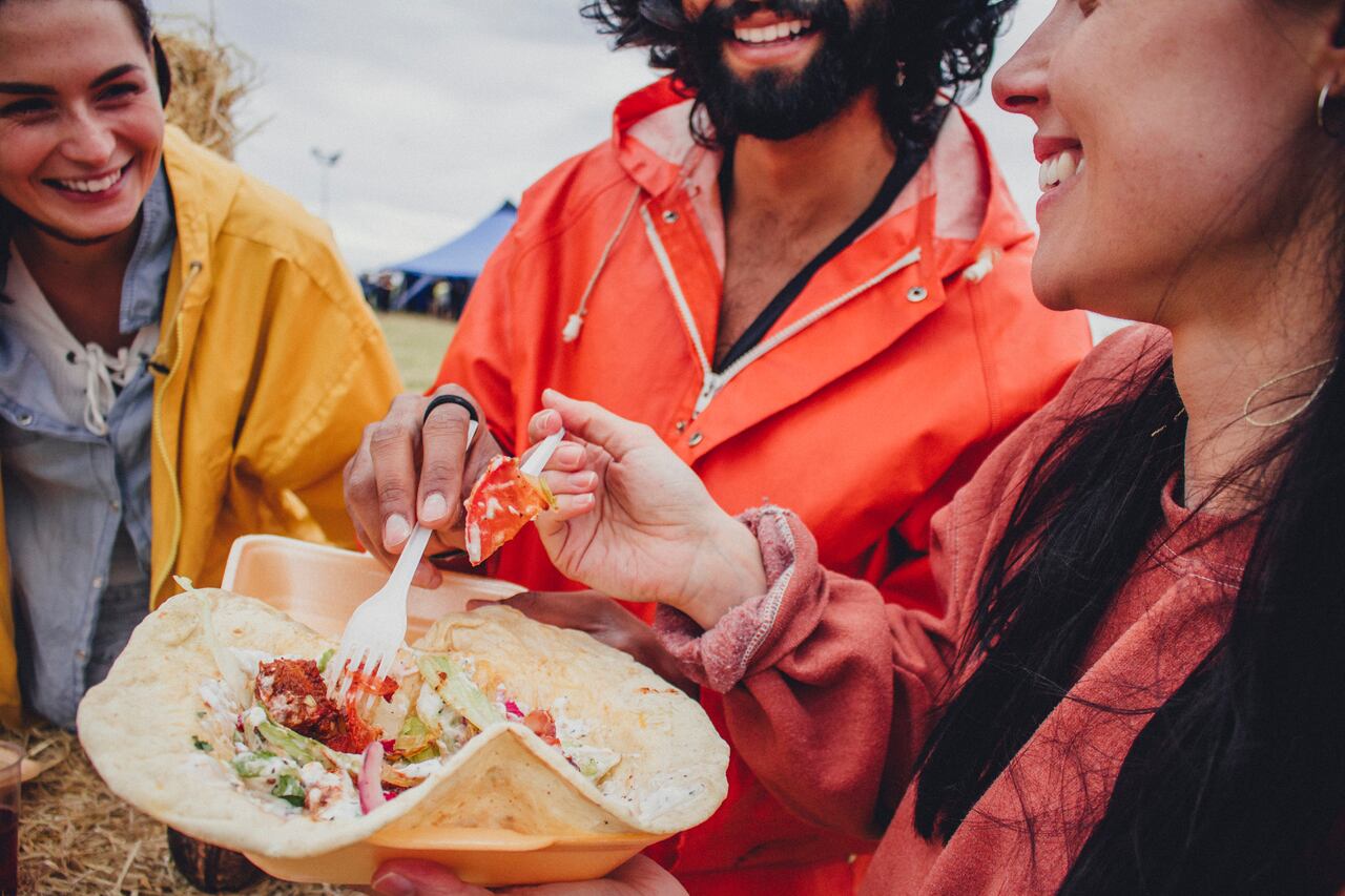 Three friends enjoy sharing some take away food while at a music festival