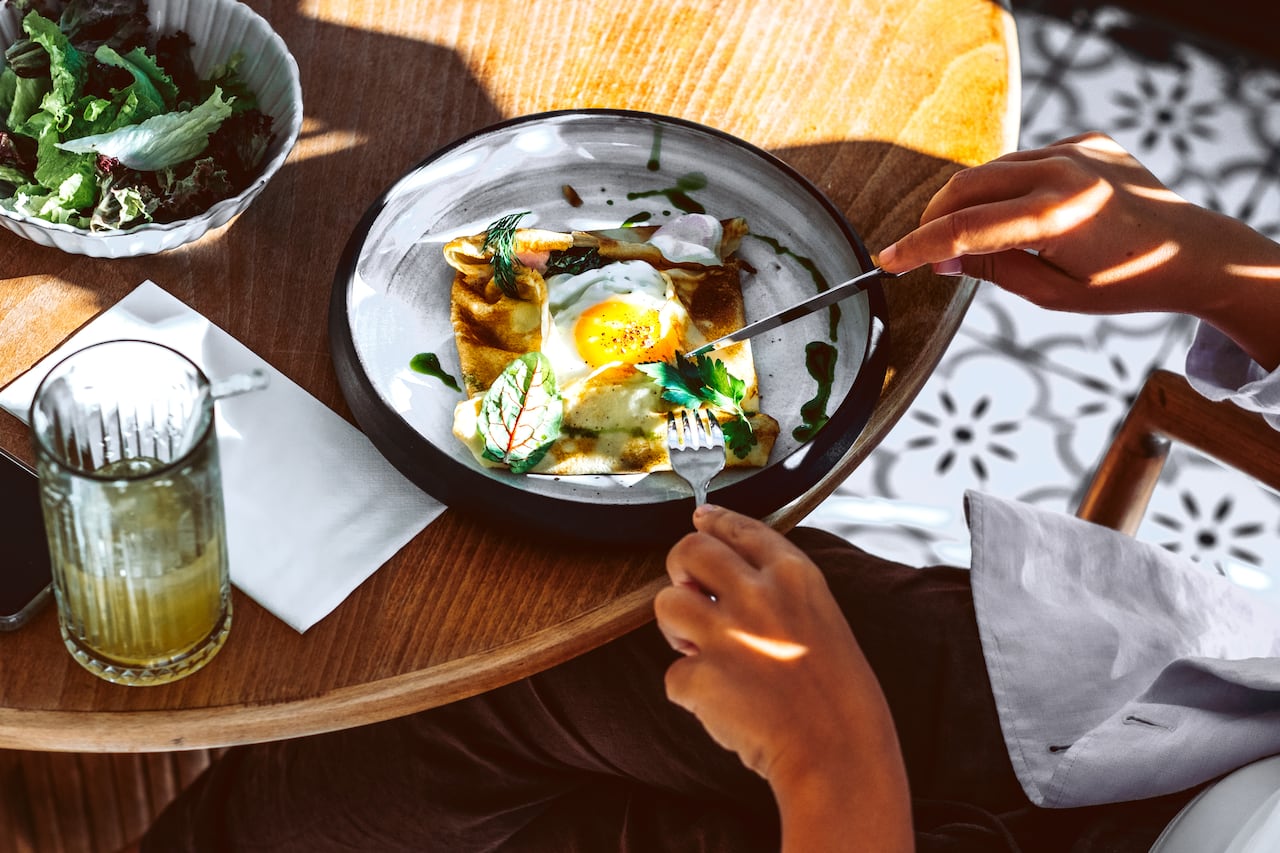 Top view of savory crepe with sunny side egg herbs and sauce on ceramic plate in warm sunlight. Concept of gourmet brunch experience and stylish food presentation.