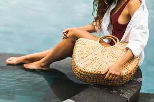 Woman near swimming pool holding in hands handmade straw wicker beach bag. Eco-friendly and zero waste tropical lifestyle. Organic and natural, plastic free.