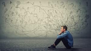 Un adolescente molesto y cansado sentado en el suelo mantiene la mano en la mejilla mirando pensativo y sin esperanza. El estudiante estresado siente incomodidad emocional, ansiedad y problemas de salud mental.