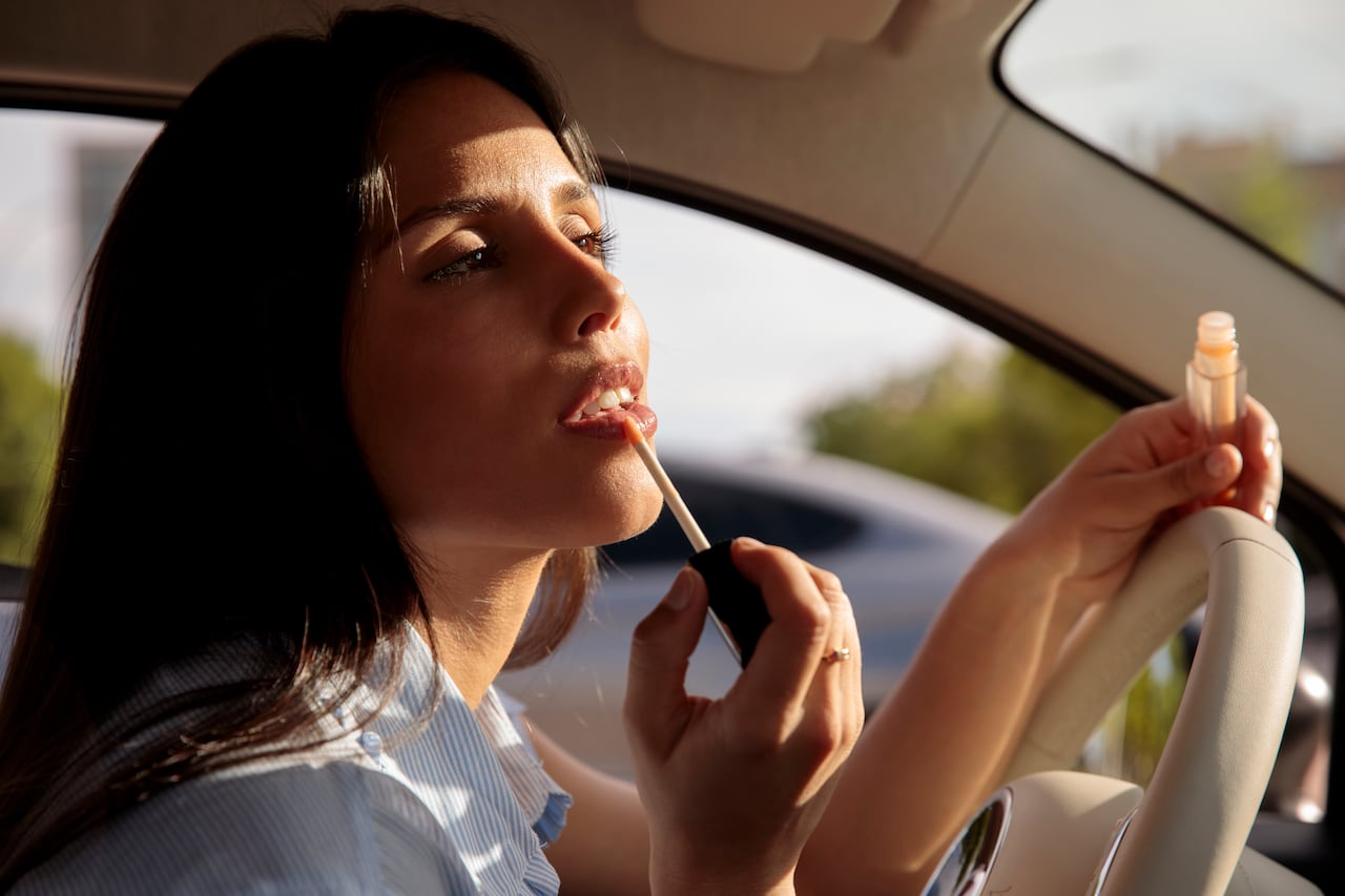 girl paints her lips reflected in the rearview mirror of the car