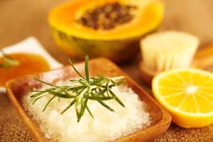 "Spa still life of organic skincare, bath sea salt exfoliation scrub, papaya, lemon, rosemary, brush, close-up"