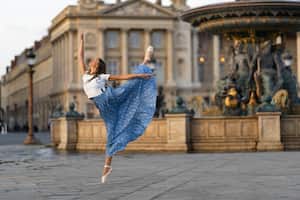 PARIS, FRANCE - MAY 01: Amanda Derhy, ballet dancer, wears a white cropped t-shirt with attached buttons, a pleated floral print pattern maxi dress, ballerina shoes and performs a ballet dance move "Attitude", during a street style fashion photo session, on May 01, 2022 in Paris, France. (Photo by Edward Berthelot/Getty Images)