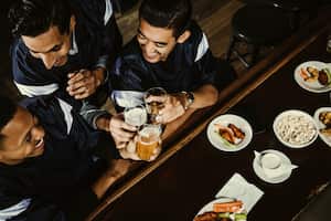 High angle view of excited sports fans toasting beer glasses at counter in bar