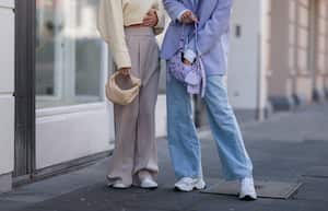 COLOGNE, GERMANY - MAY 01: Michi Brandl (L) seen wearing a pale yellow cropped pullover from Vival Studio, a gold necklace and gold earrings, a beige wide leg pants from Reserved, a beige Bottega Veneta bag and white sneakers from Nike and Justine Schlütter seen wearing a pale purple oversize blazer, a purple bra from Mango, a blue denim wide leg jeans, a purple Balenciaga Cargole Mini leather bag and white leather sneakers from Nubikk on May 01, 2022 in Cologne, Germany. (Photo by Jeremy Moeller/Getty Images)