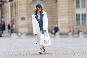 PARIS, FRANCE - APRIL 16: Natalia Verza @mascarada.paris wears a Nike cap hat, a gray striped oversized blazer jacket, a metallic chain necklace, a gray t-shirt, a white long oversized coat, white midi leggings, a white quilted leather Chanel bag, Dior monogram printed ankle sneakers shoes, on April 16, 2021 in Paris, France. (Photo by Edward Berthelot/Getty Images)