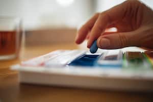 Close up photo of woman hands taking her daily vitamins and supplements from pill box on the table.