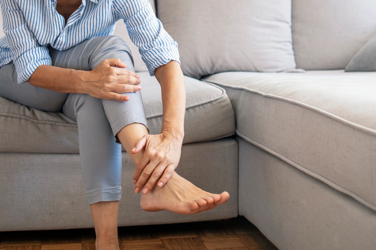 Closeup young woman feeling pain in her foot at home. Healthcare and medical concept. Tired and aching female feet after walking. Woman with feet intense pain sitting on a couch at home.