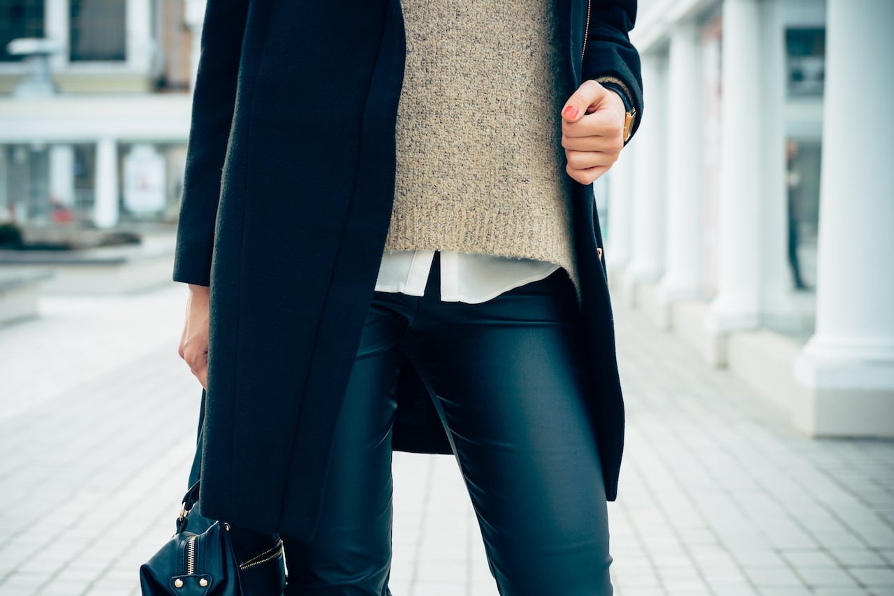 Details of women's clothing. Close-up of a woman in a sweater, coat, black pants. In her hand female bag.