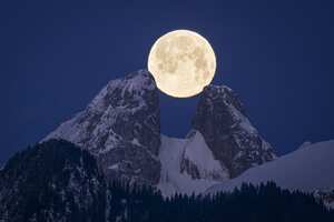 La luna llena se pone detrás de las montañas, incluidos los picos gemelos de Les Jumelles en Chablais Valaisan, cerca de Aigle, Suiza, el lunes 6 de febrero de 2023.