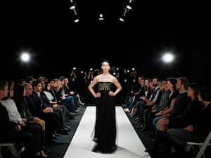 Model in gown walking down catwalk during fashion show photographers and crowd in background