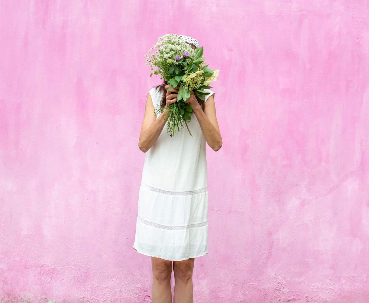 Woman in a white dress with a bouquet of flowers covering her face