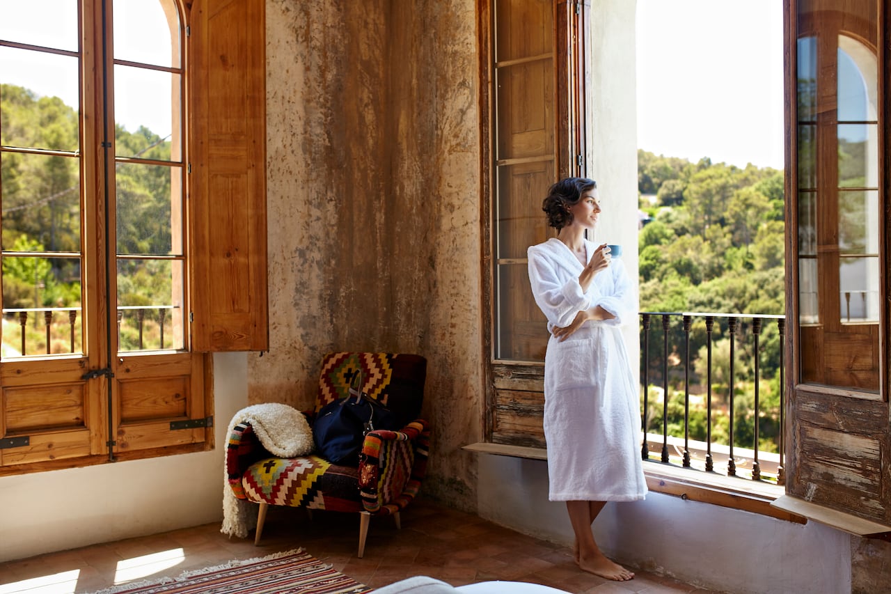 Thoughtful woman having coffee while looking through window in hotel room