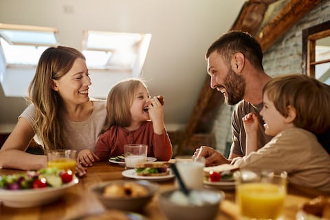 Young parents and their small kids talking while having breakfast in dining room.