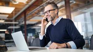 Profesional de negocios de adultos medianos sentado en la mesa con una computadora portátil y hablando por teléfono móvil. Empresario trabajando en oficina.