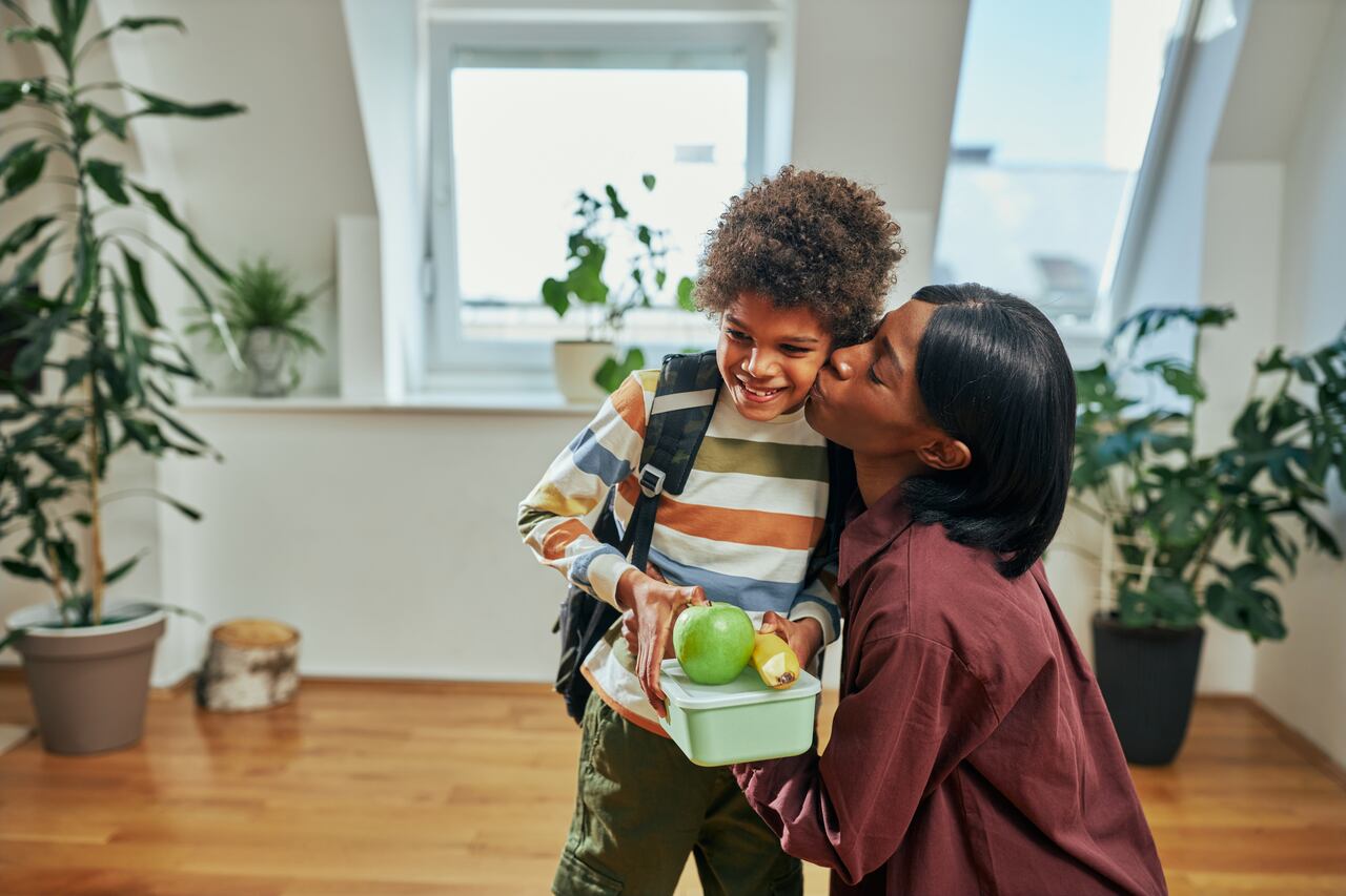 African mother giving lunch box to her schoolboy and kissing him