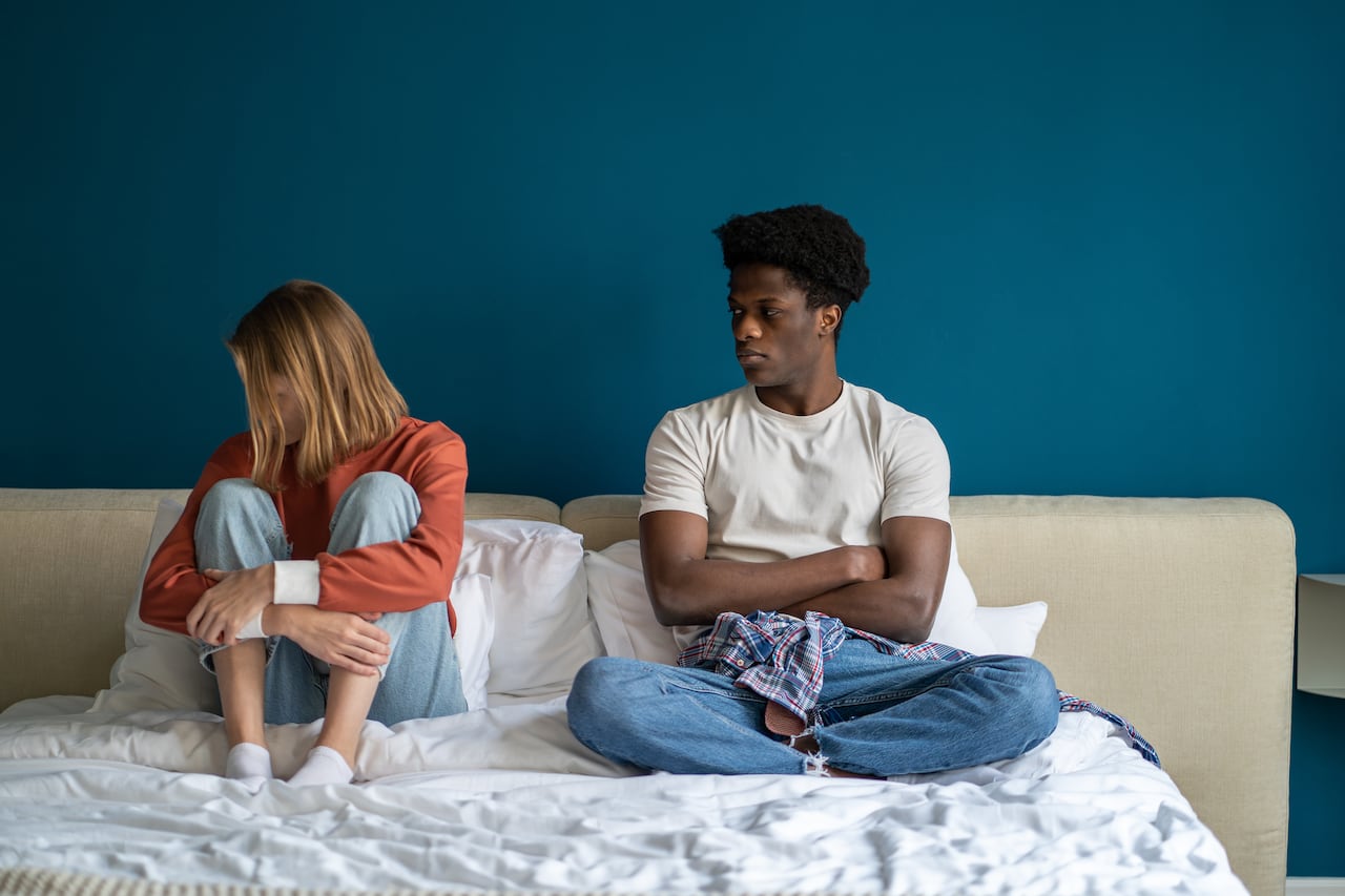 Girl offended by guy sit in bed at home, couple conflict quarrel in relationships. Caucasian blonde woman ignoring african american man turning head away. Misunderstanding relationship crisis problem.
