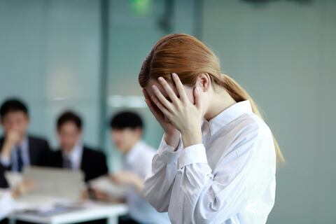 Stressed Businesswoman at desk,colleagues in background having discussion