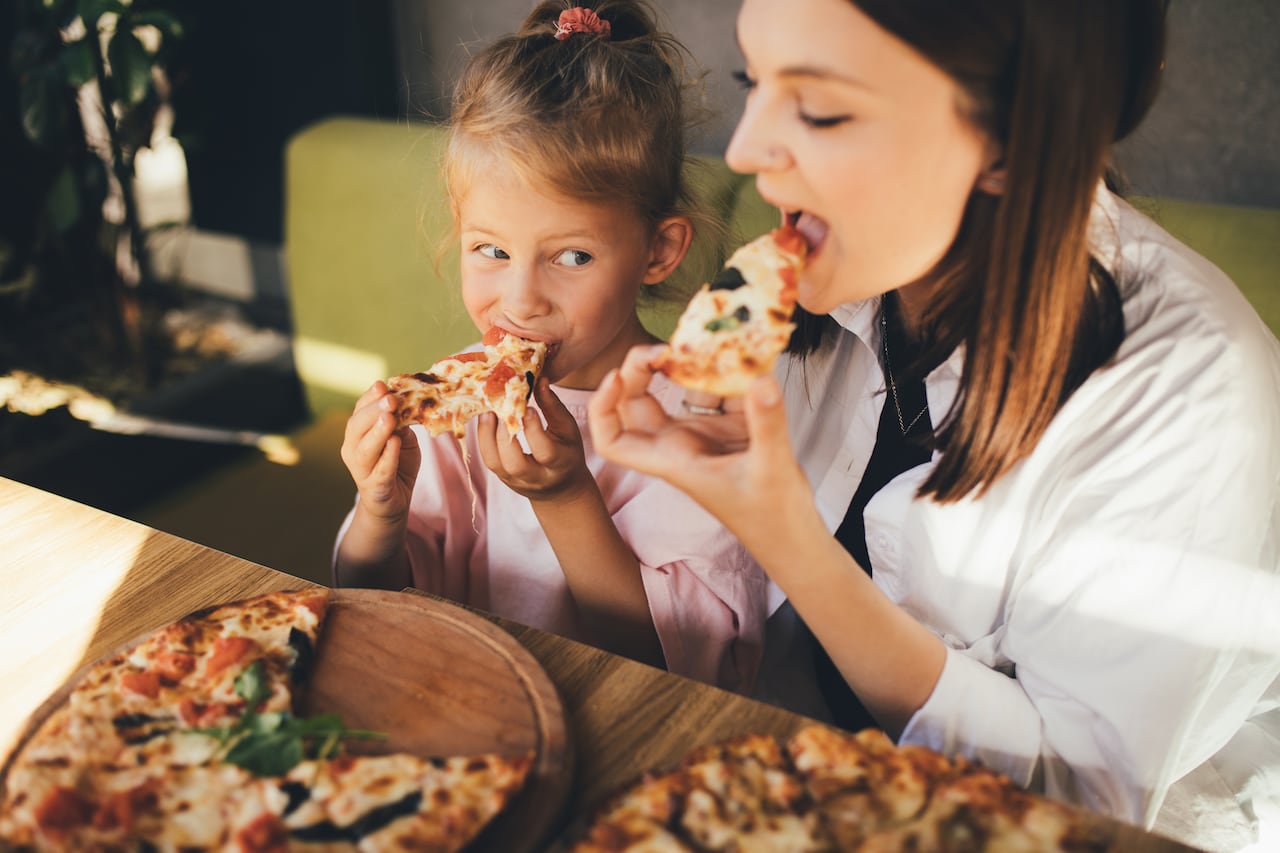 Mother and daughter eat pizza in a cafe.