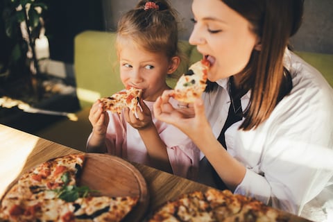 Mother and daughter eat pizza in a cafe.