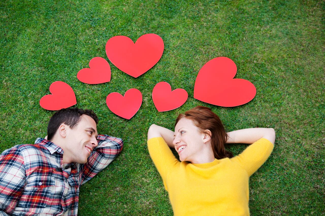 Couple laying in grass,surrounded by hearts.