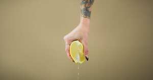 Studio shot of an unrecognizable woman squeezing a lemon slice against a brown background