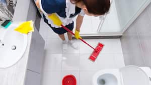 Ama de llaves o sirvienta con uniforme limpio y delantal de pie fregando el suelo en un baño visto desde arriba