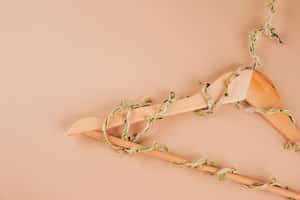 Wooden hangers entwined with plants on biege background with copy space. Conscious and environmentally friendly consupmtion - new modern trends in shopping. Zero waste, slow fashion concept.