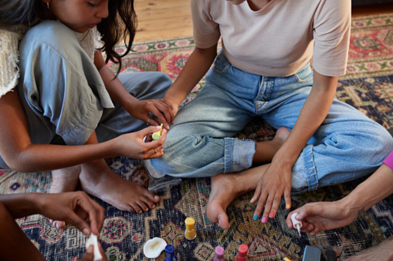 High angle view of woman applying multi colored nail polish to friend at slumber party